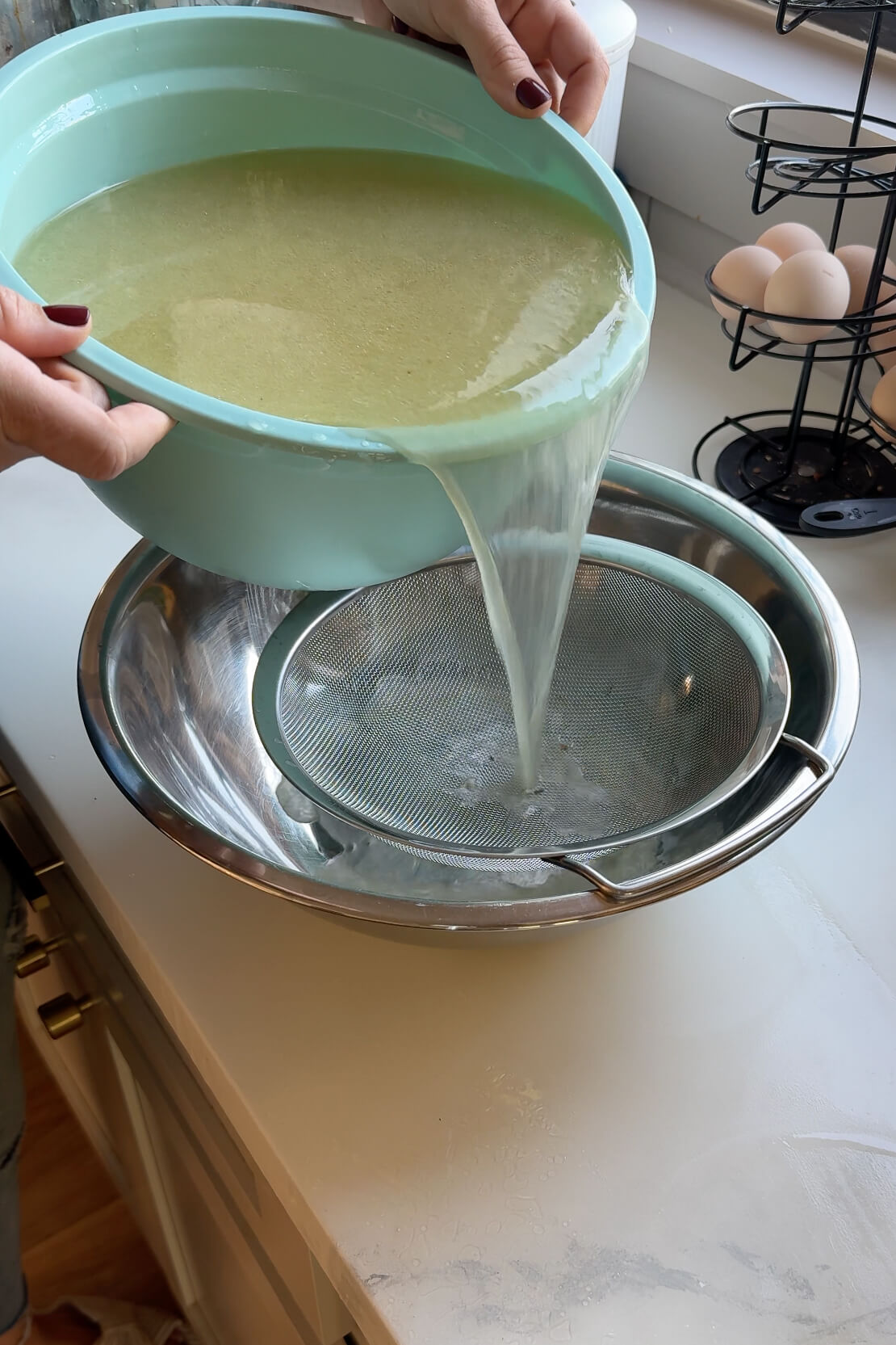 Straining homemade chicken broth through a fine mesh strainer.